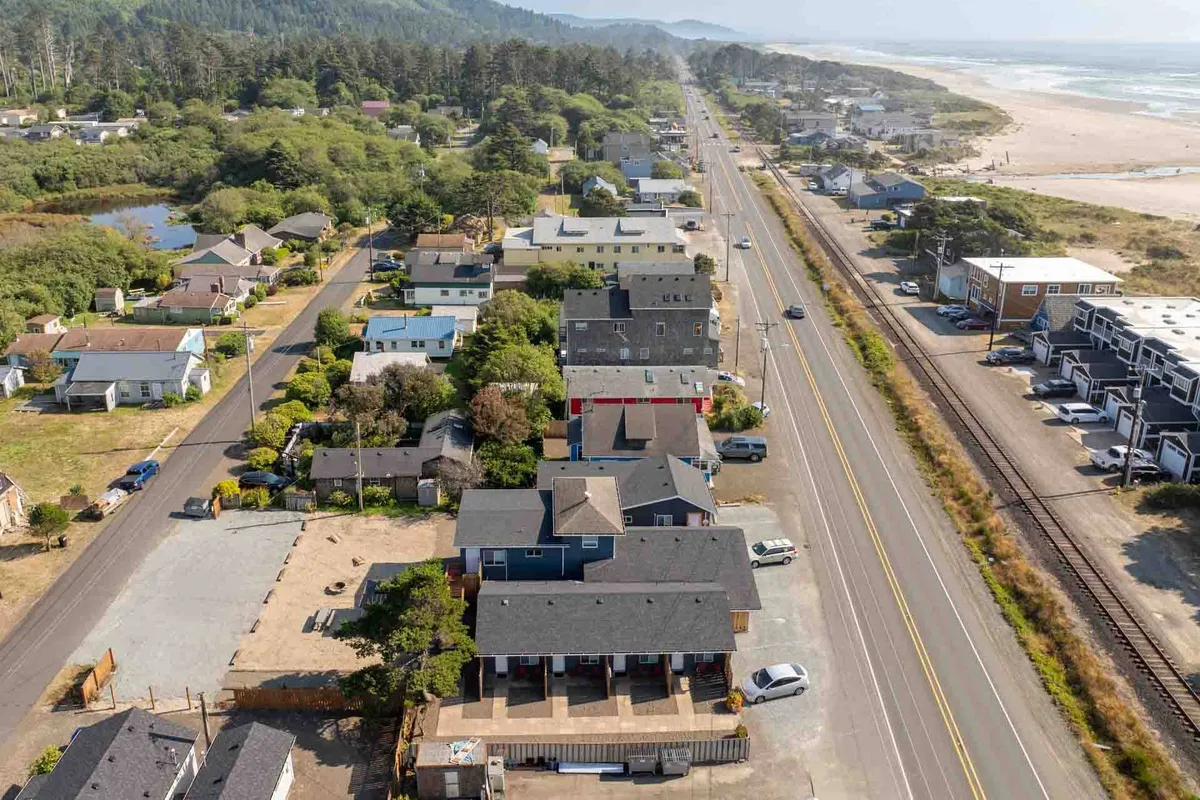 This exterior scene captures residential buildings nestled near a beach, with a road invitingly leading into the heart of the local area. The natural landscape, including sand dunes and greenery, creates an inviting and accessible atmosphere, while subtle hints of community activity suggest nearby shops and gathering spots.