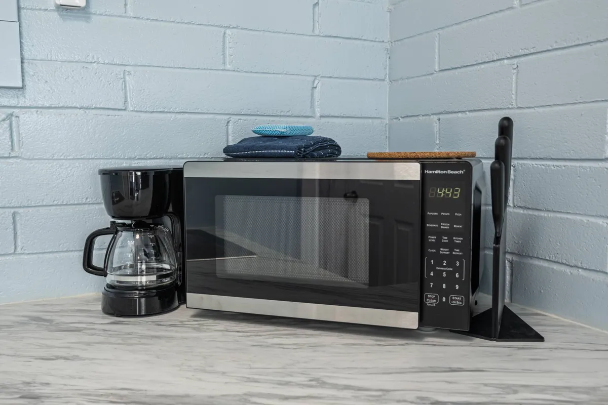A closer view of the kitchen area, featuring a microwave, coffee maker, kitchen towels, and a cutting board. The countertop appears ready for meal preparation, and the warm lighting creates a cozy, homey ambiance.