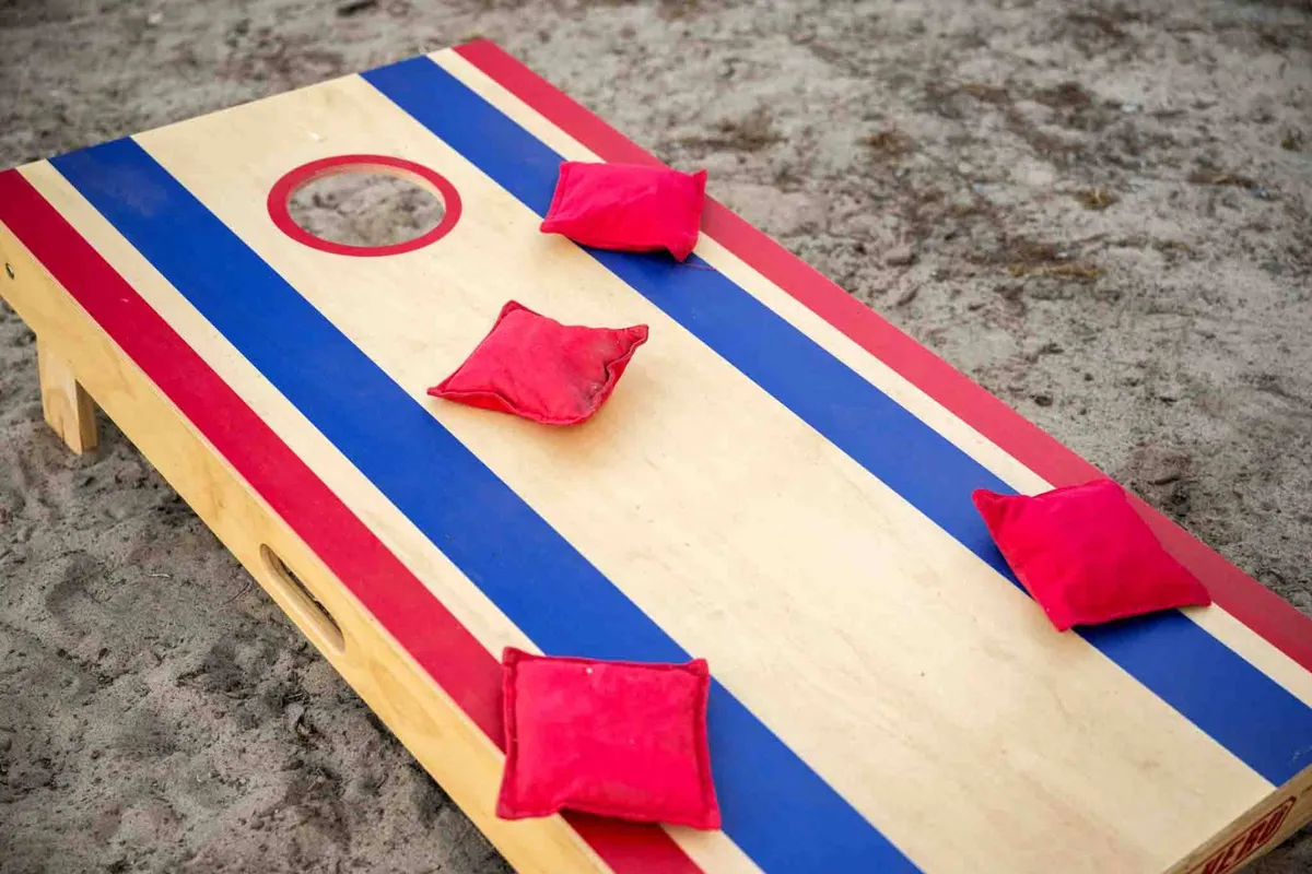 A vibrant outdoor scene featuring a cornhole board with bright red bean bags set up on a grassy area, inviting guests to engage in playful, family-friendly activities. The image suggests a communal space ideal for mingling and creating memories.